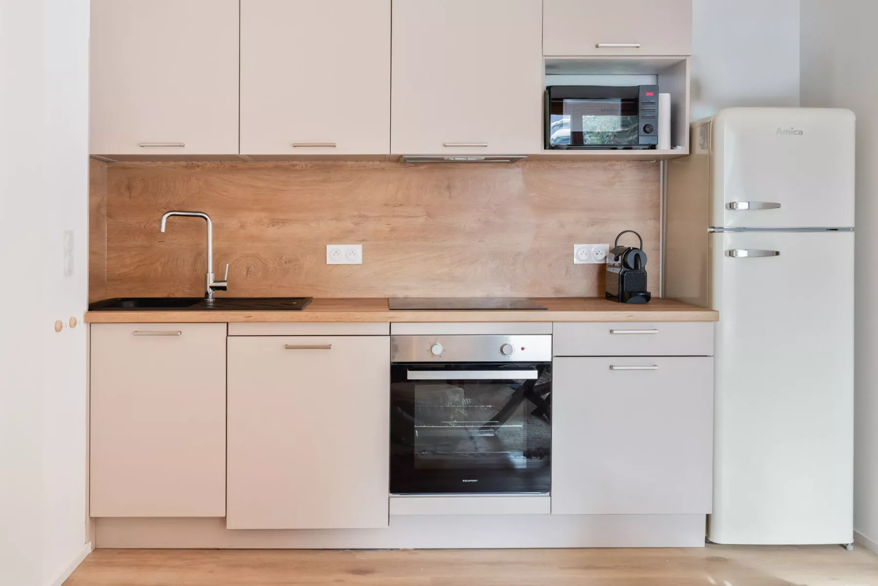 Una cocina moderna con armarios claros, un salpicadero de tono madera y electrodomésticos integrados.