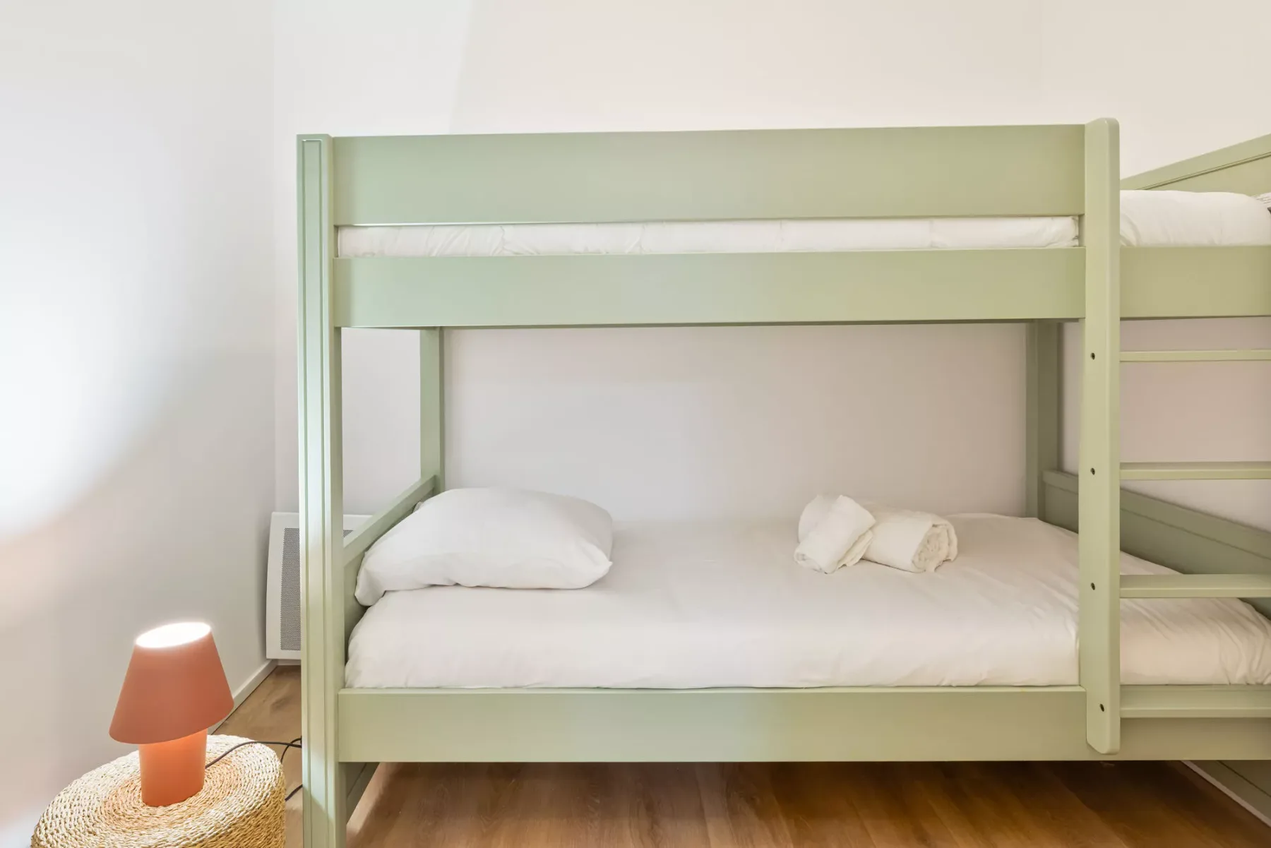 A pale green bunk bed with pillows stands against a light-colored wall.