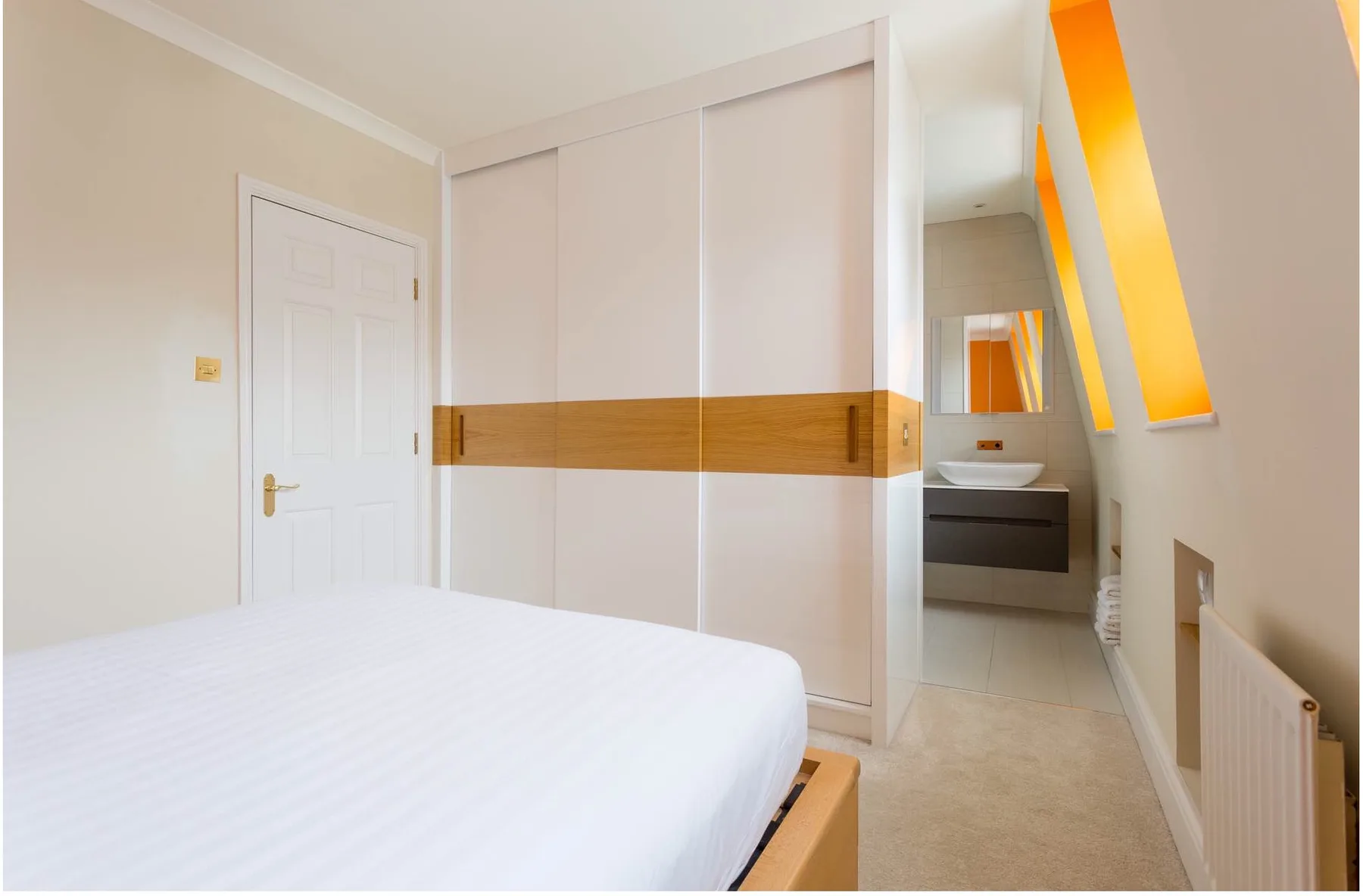 Un dormitorio con una cama junto a un armario empotrado y una zona de lavabo abierta.