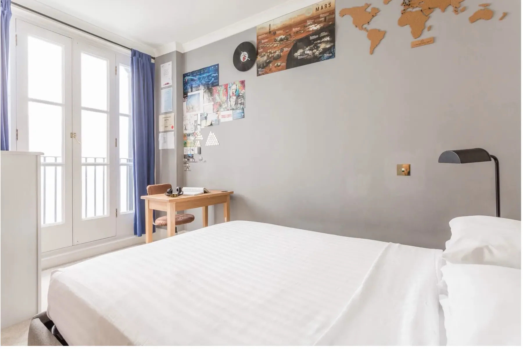 Un dormitorio con una cama, un escritorio pequeño y puertas acristaladas altas.