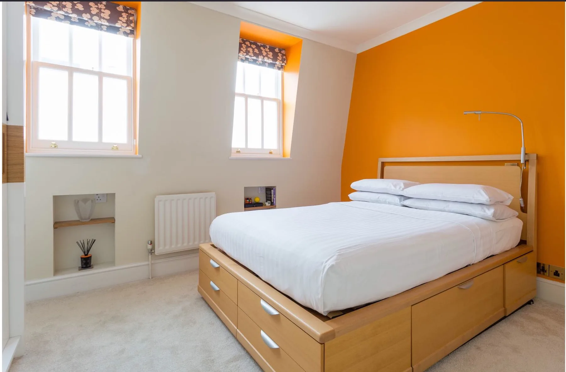 Un dormitorio con una cama de madera, ropa de cama blanca y una pared naranja.