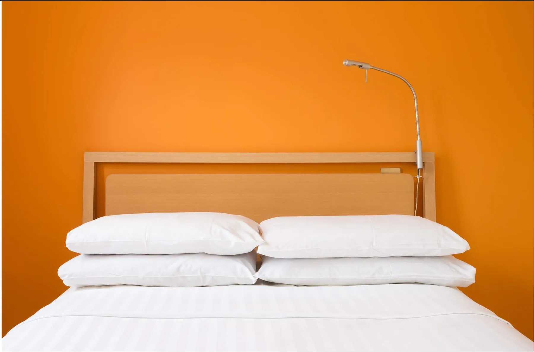 Un dormitorio con almohadas blancas ordenadas frente a una pared naranja.