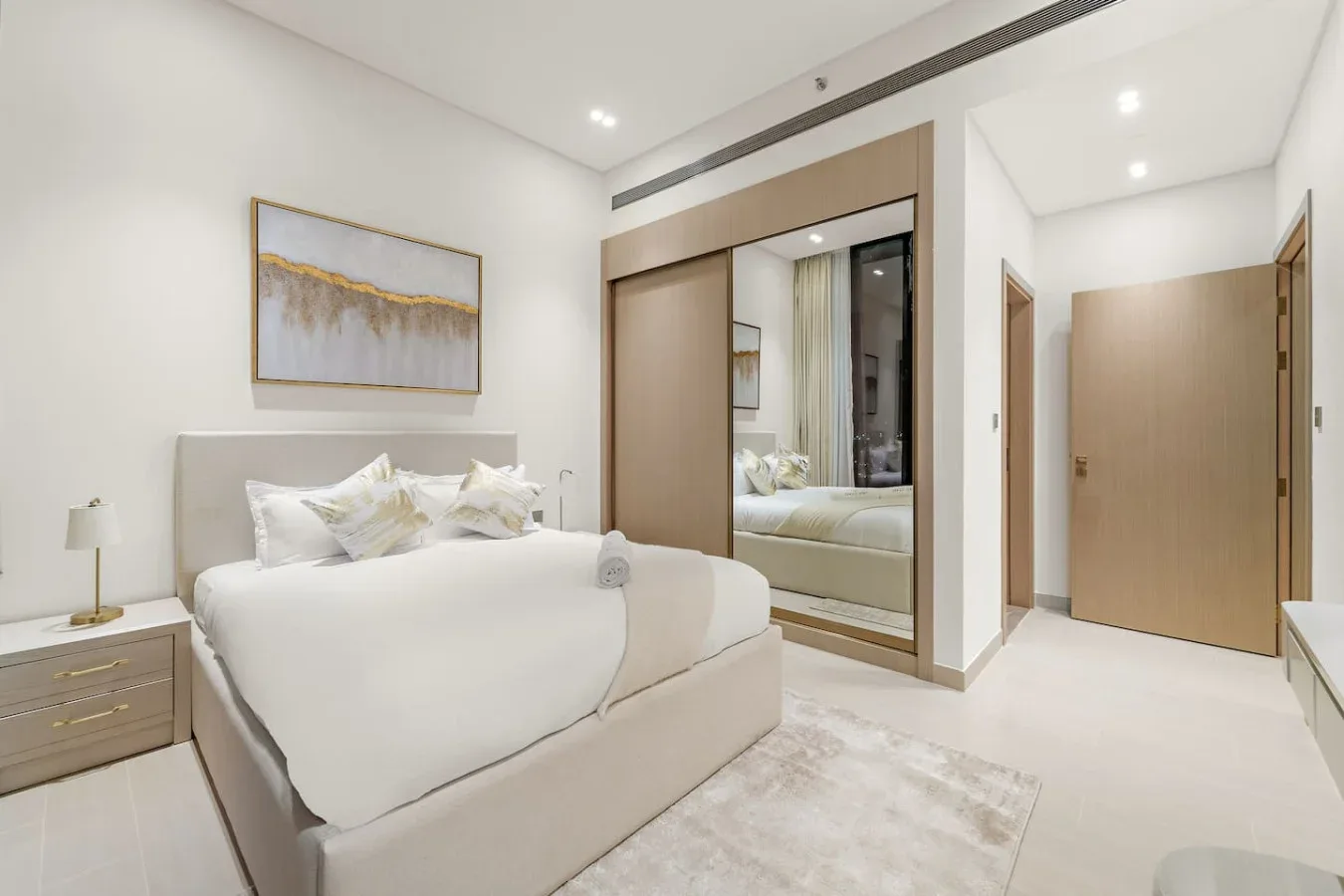 Un dormitorio luminoso con una cama tendida y un armario con espejo.