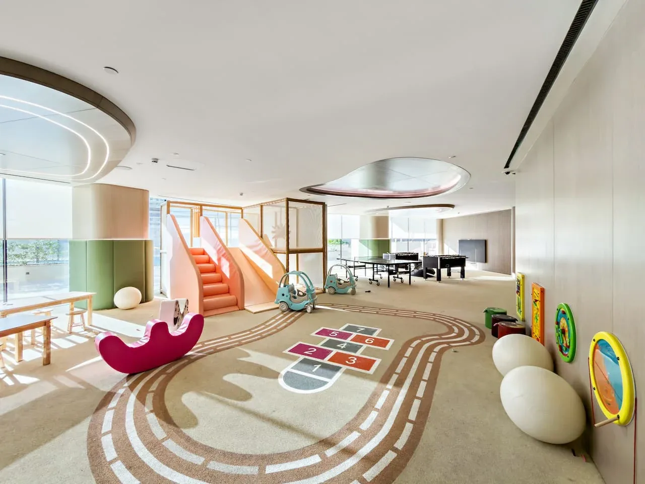 Una luminosa zona de juegos interior tiene un recorrido colorido en el suelo y una mesa pequeña.