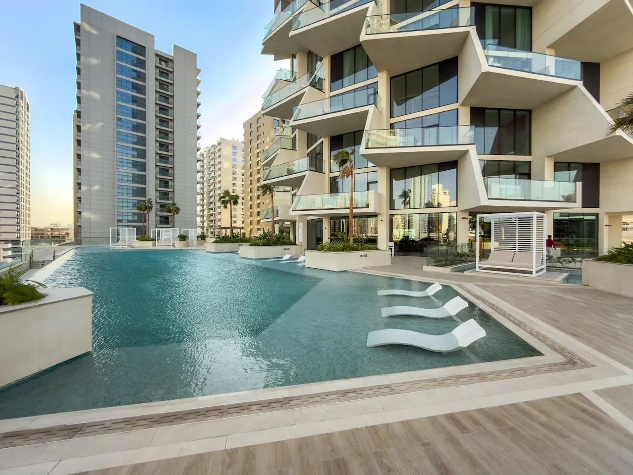 Una piscina junto a un edificio de apartamentos moderno con balcones.