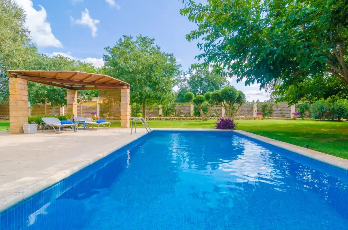 An outdoor swimming pool beside a shaded seating area and landscaped garden.