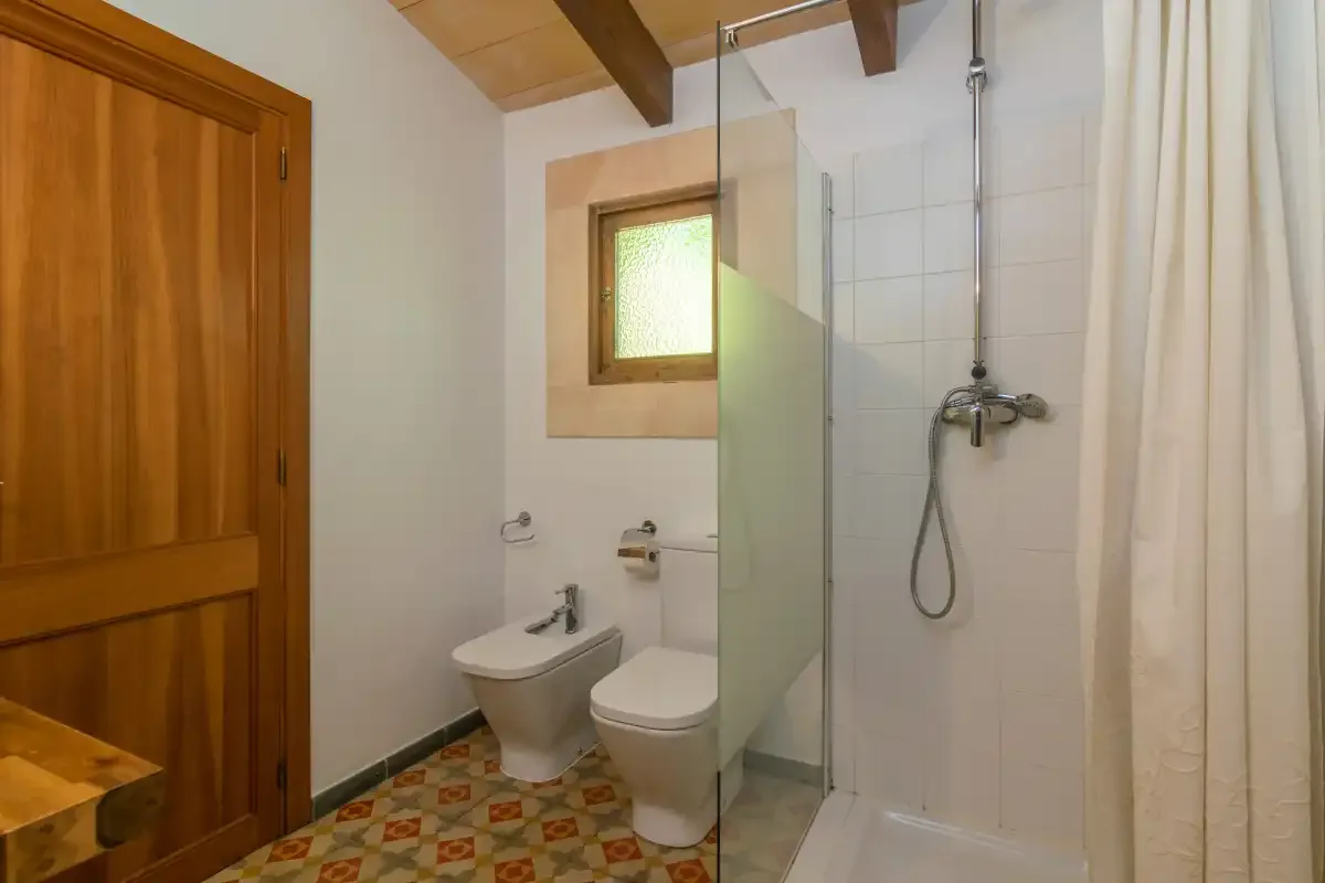 A bathroom with a shower, toilet, and small frosted window.