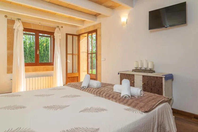 A bedroom with a bed, wooden-framed windows, and a wall-mounted television.