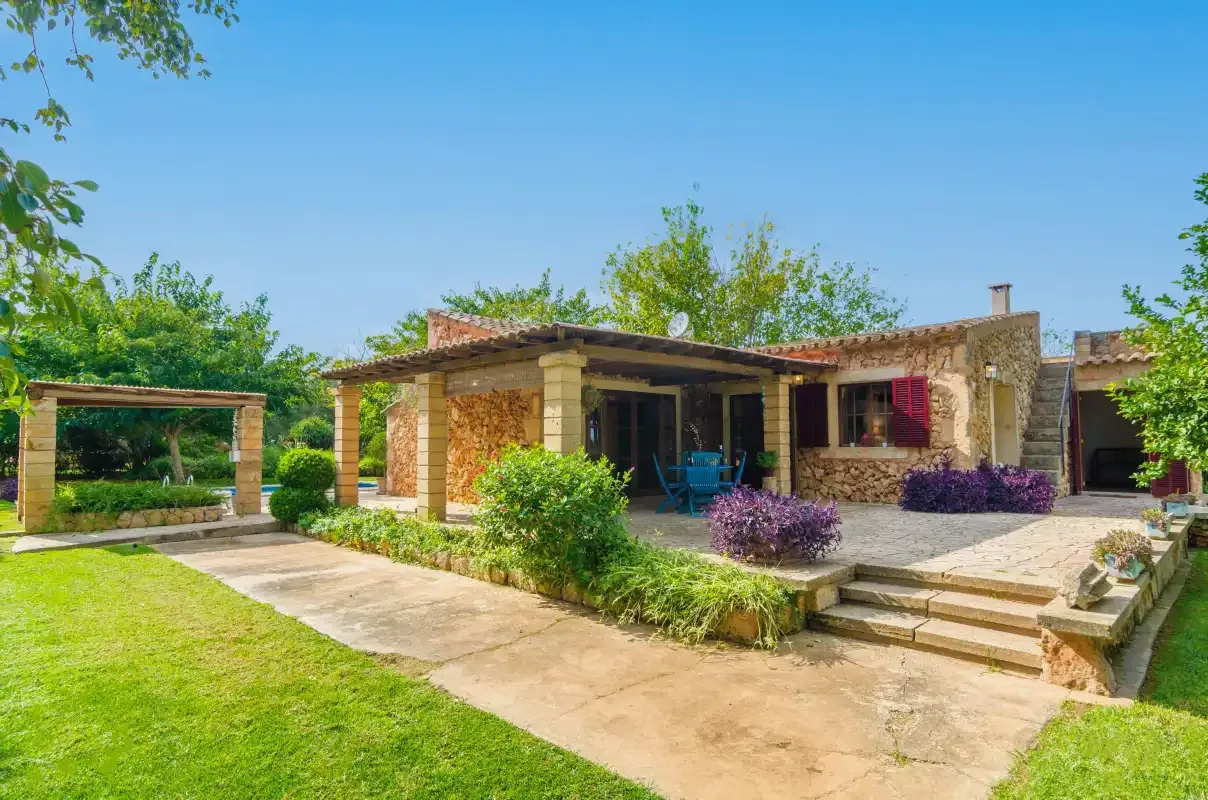 A stone house with a covered patio opens onto a sunny lawn.
