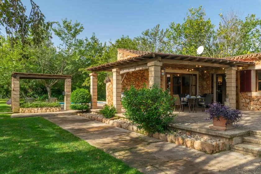 A stone house opens onto a covered patio with outdoor seating and a garden.