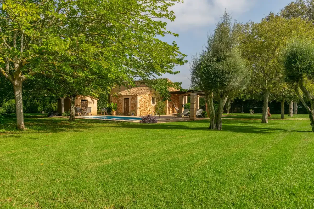 A stone building and pool sit beyond a broad green lawn among mature trees.