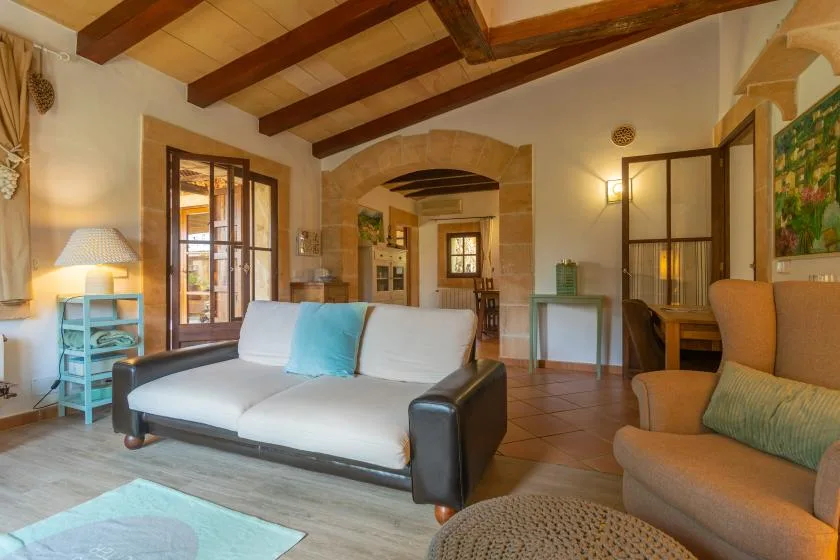 A living room with seating, exposed wooden ceiling beams, and an arched doorway.