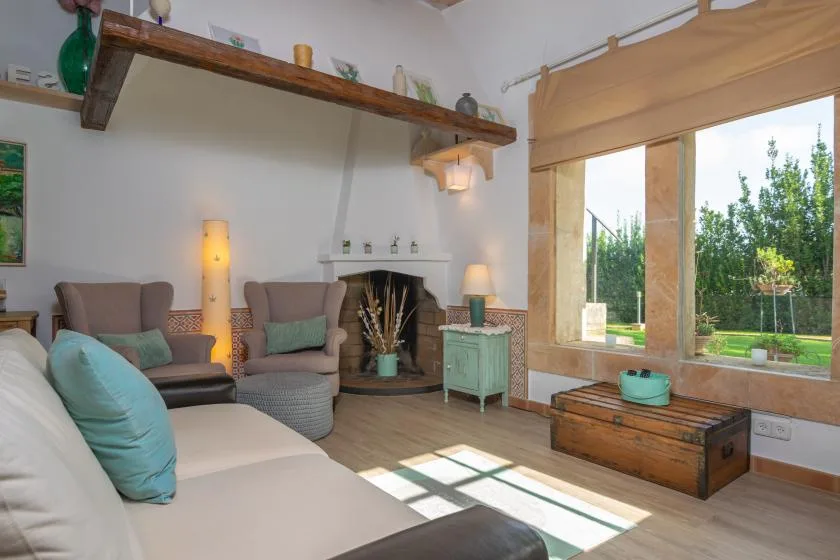 A bright living room with seating, a fireplace, and large windows overlooking greenery.