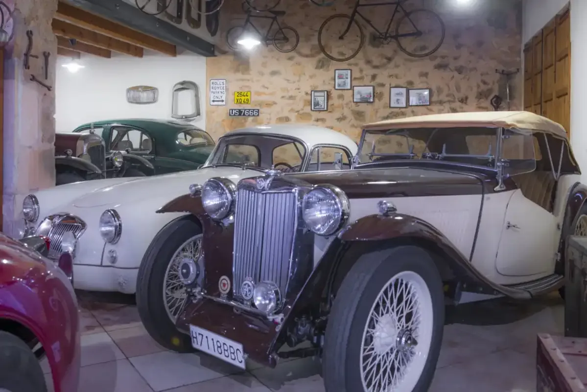 Vintage cars are displayed in a stone-walled garage.