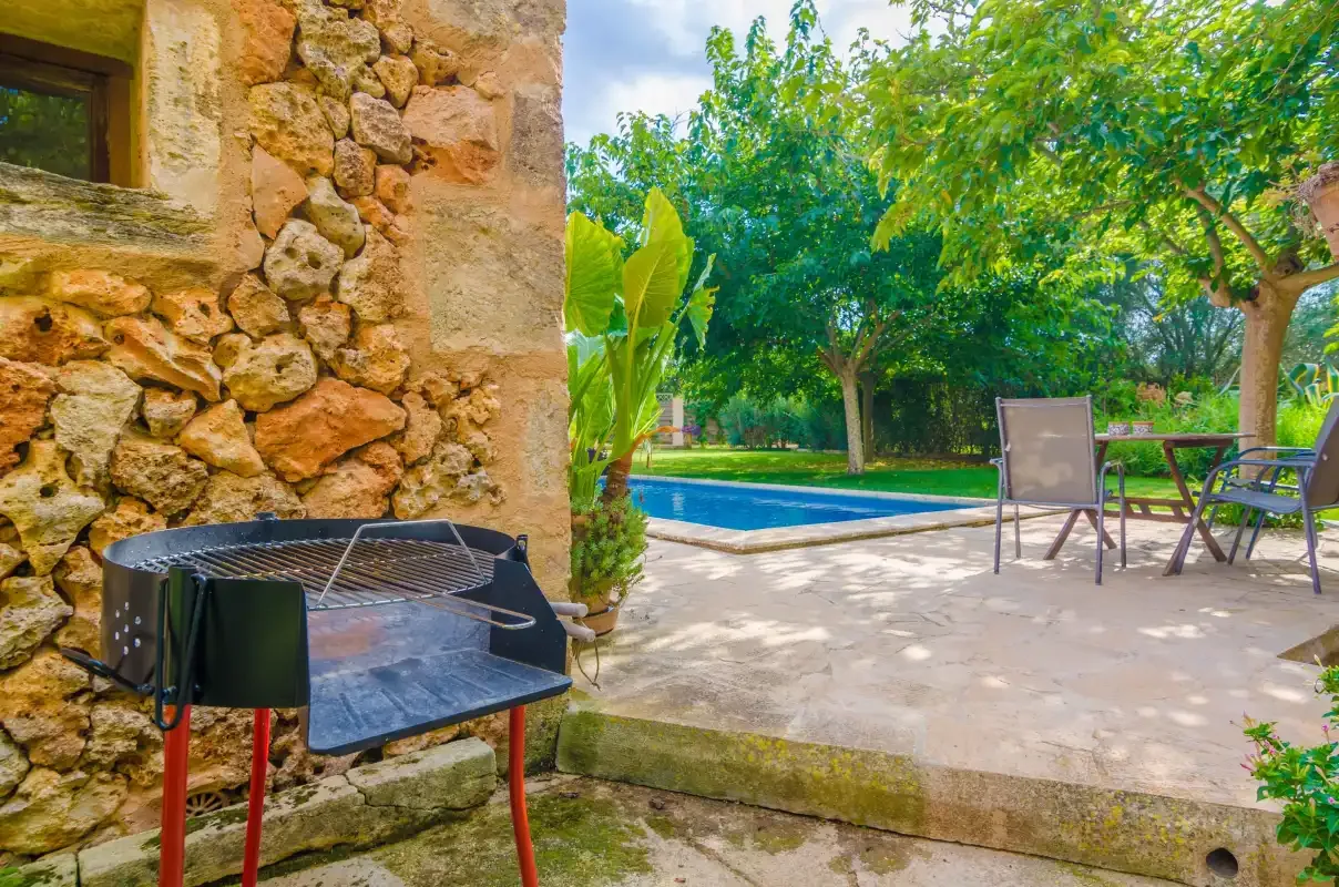 An outdoor pool and patio sit beside a stone wall and leafy trees.