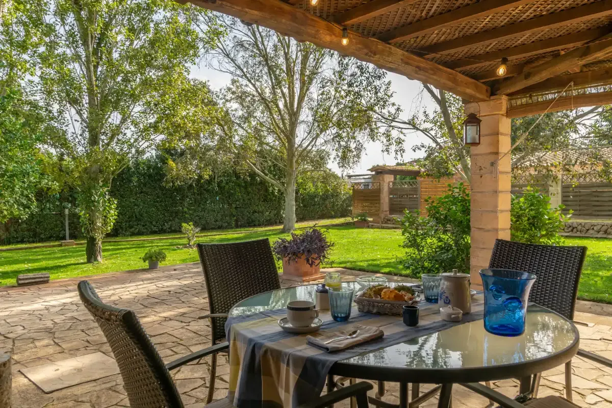 A covered patio dining area overlooks a green garden with trees and shrubs.