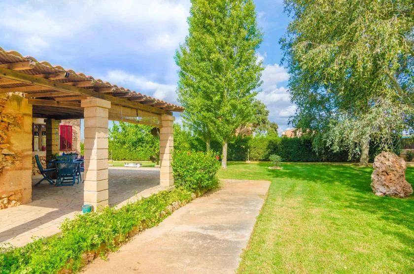 A garden path runs beside a covered patio with seating and trees.