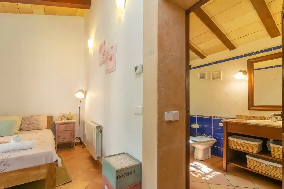 A bedroom opens onto a bathroom with blue tile and a wooden vanity.