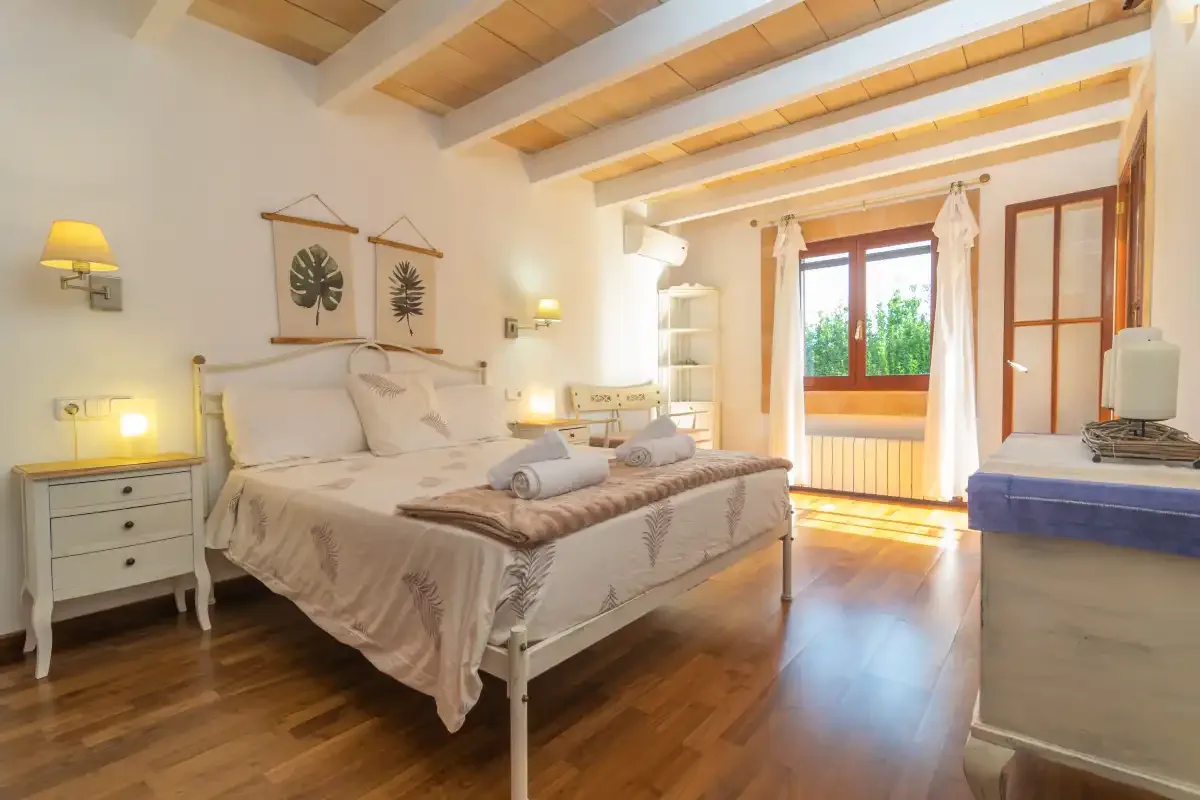 A bedroom with a bed, bedside tables, and a window overlooking greenery.