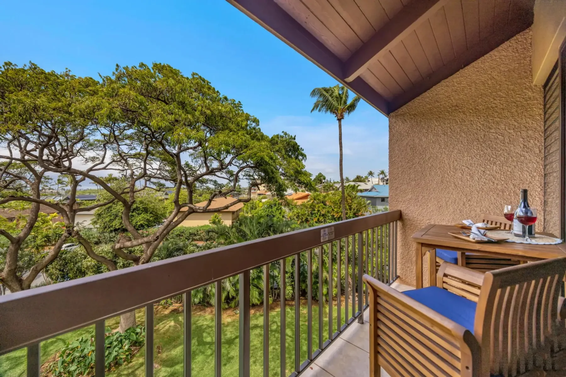 A covered balcony overlooks leafy trees, with a small table and seating.