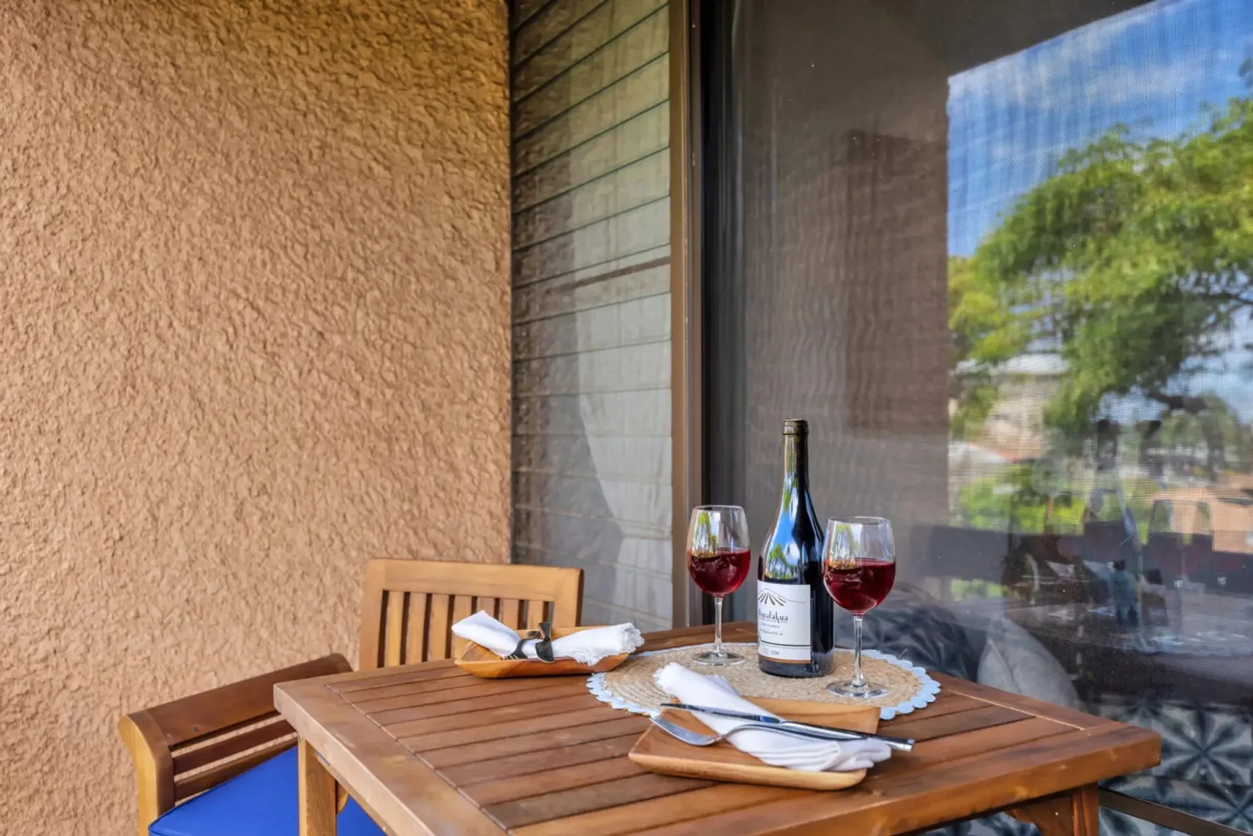 A small outdoor dining table is set with plates and glasses beside a window.