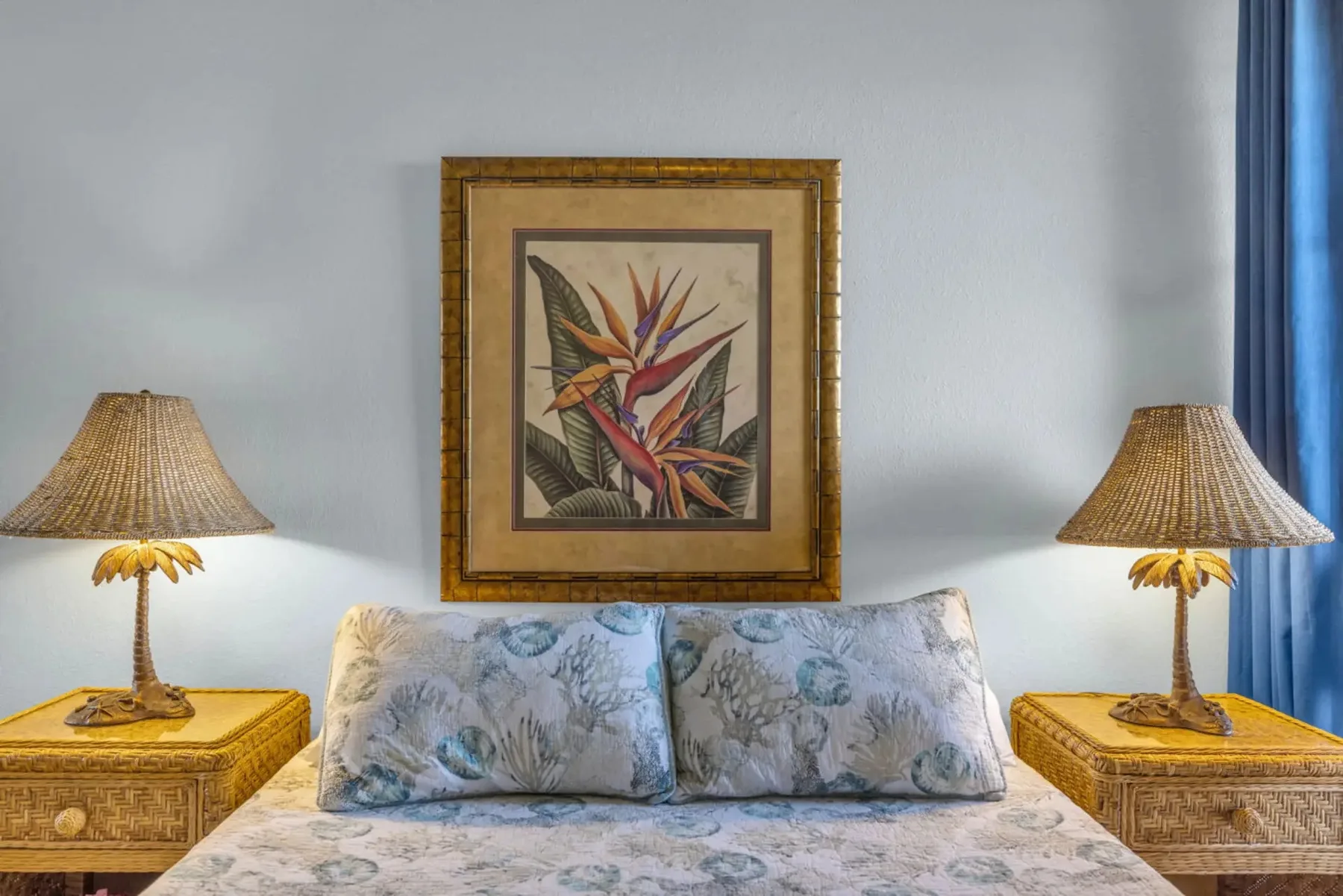 A bedroom with a bed beneath framed botanical artwork and matching bedside lamps.