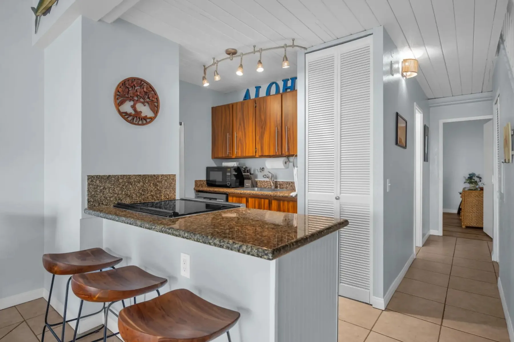 A bright kitchen with a breakfast counter and wooden cabinets beside a hallway.