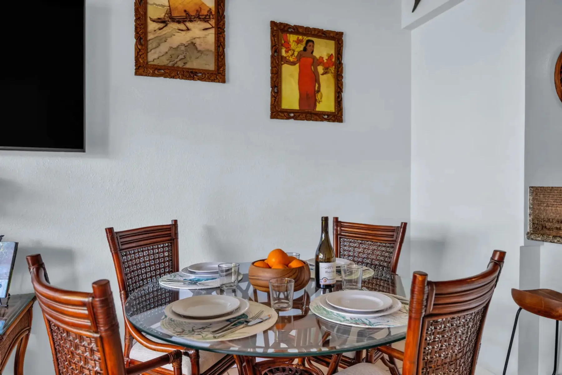 A dining area with a glass table, wooden seating, and framed wall art.