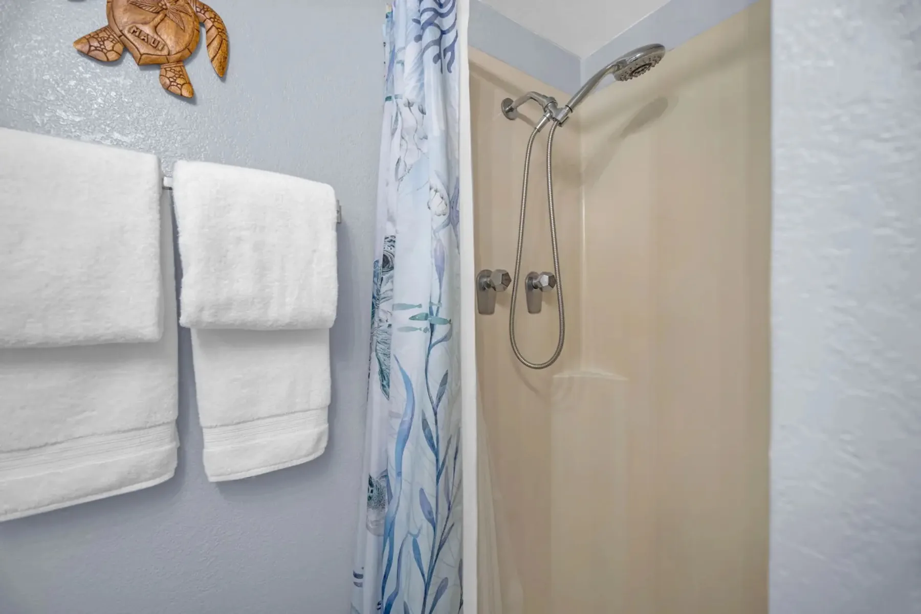 A bathroom shower with a patterned curtain and white towels hanging nearby.