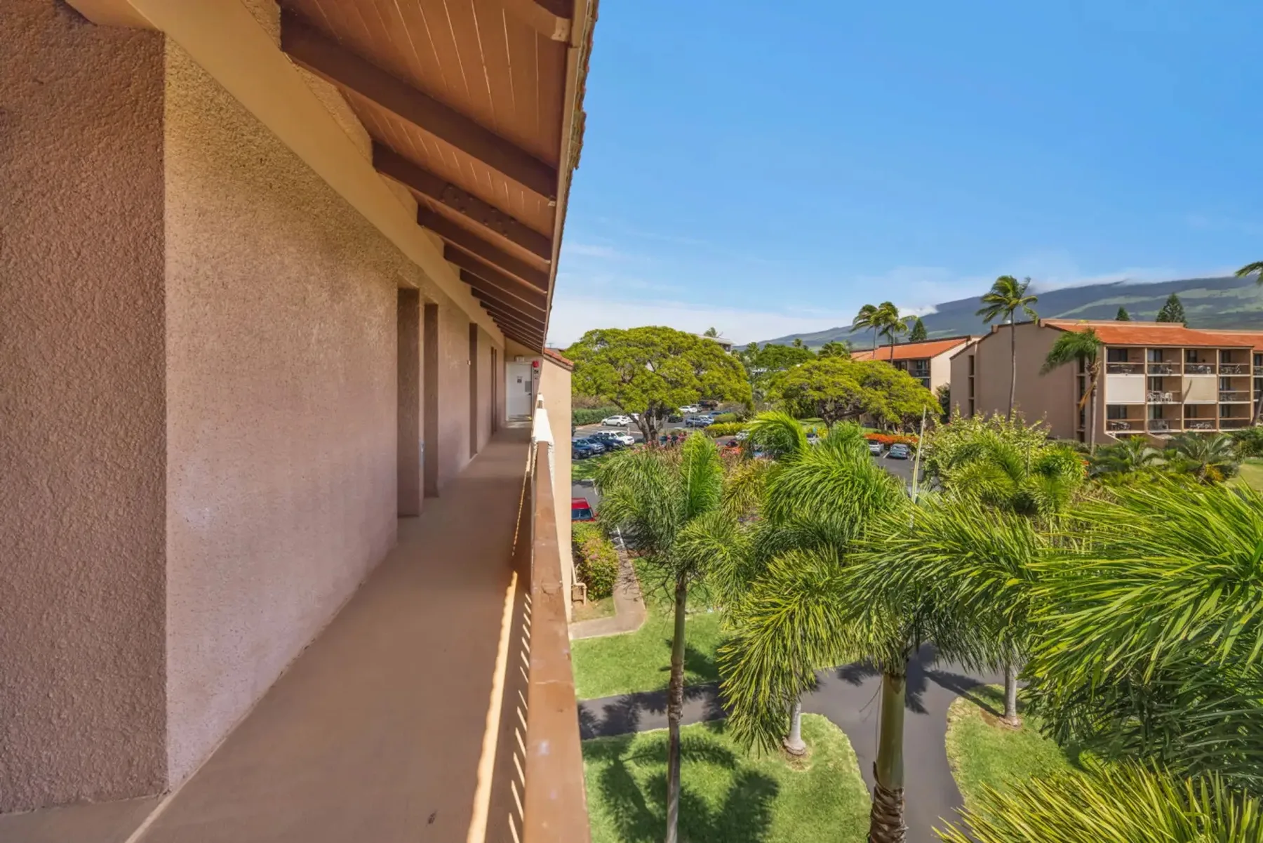 A covered outdoor walkway overlooks palm trees and landscaped grounds.