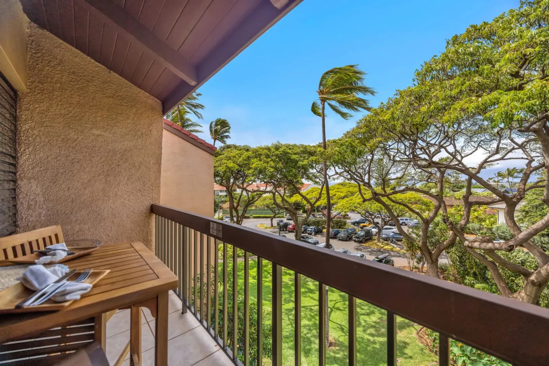 A balcony dining area overlooks leafy trees and a parking lot.