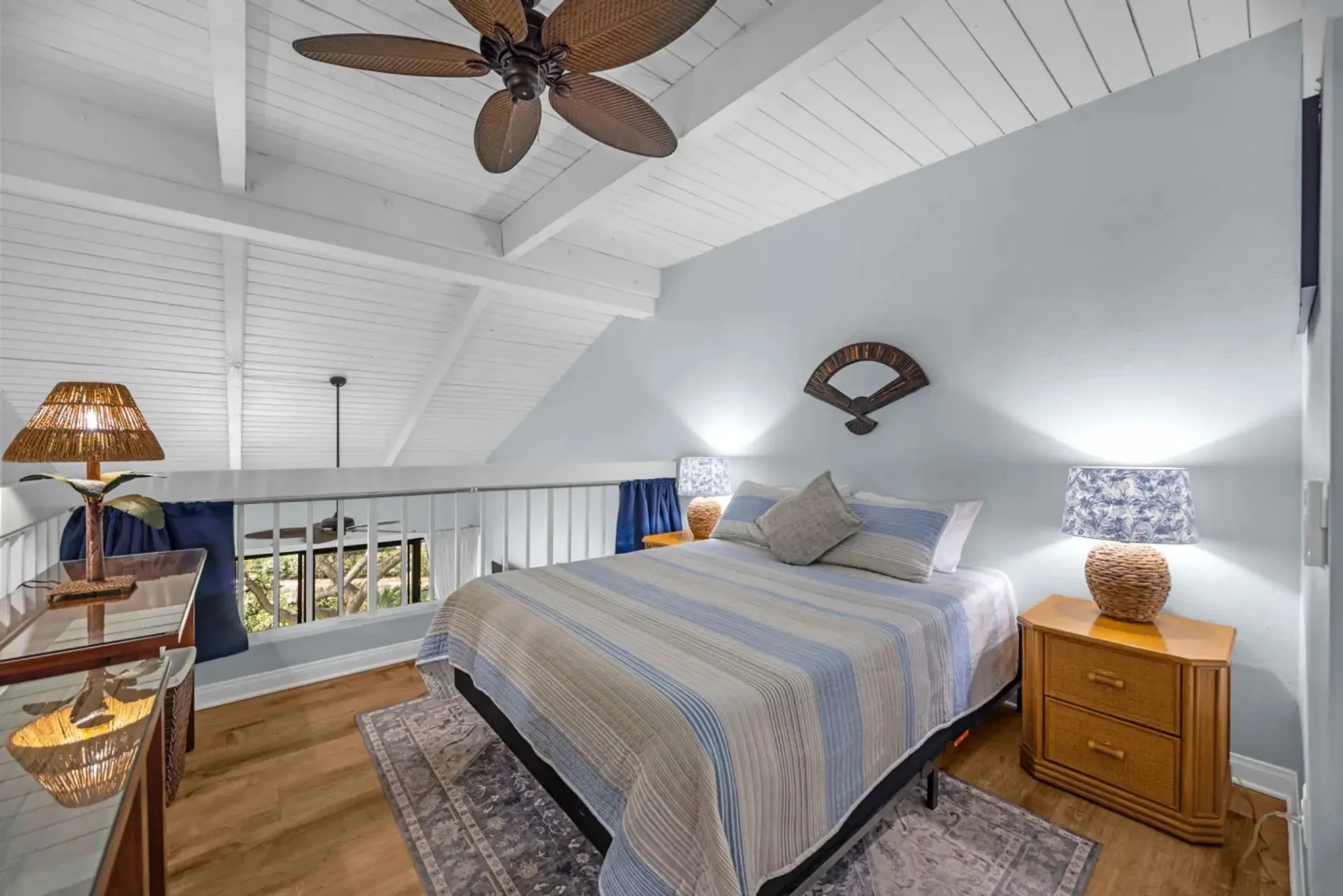 A bedroom with a bed beneath a sloped, white-beamed ceiling.