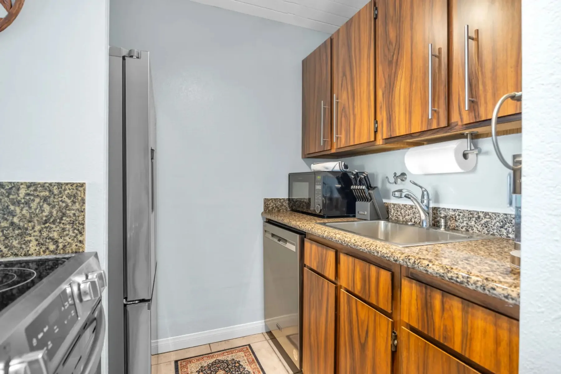A compact kitchen with wooden cabinets, granite counters, and stainless steel appliances.
