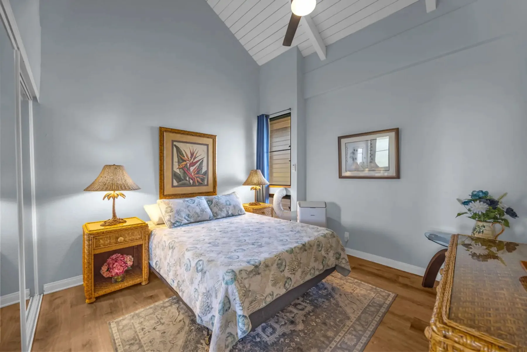 A bedroom with a bed, bedside tables, framed artwork, and a high sloped ceiling.