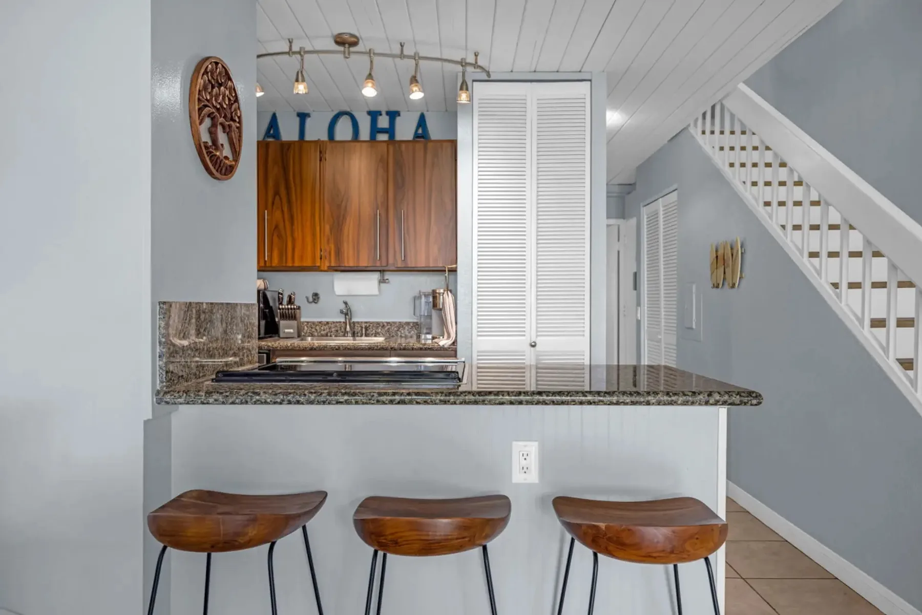 A kitchen counter with wooden stools sits beneath a staircase.