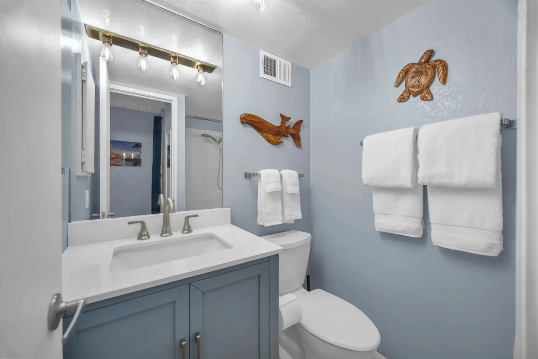A bathroom vanity and toilet sit beneath a mirror, with towels hanging on the wall.