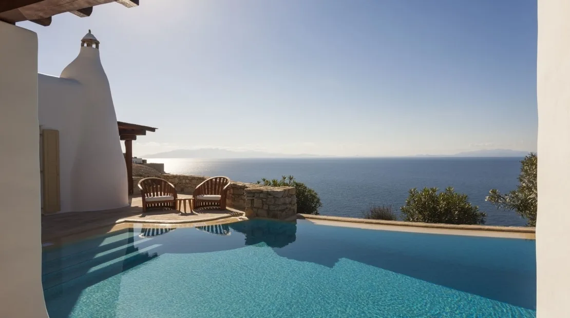 A swimming pool overlooks the sea beside a white building.