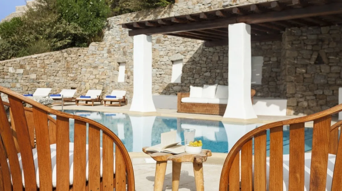 A swimming pool beside a shaded stone patio with seating.