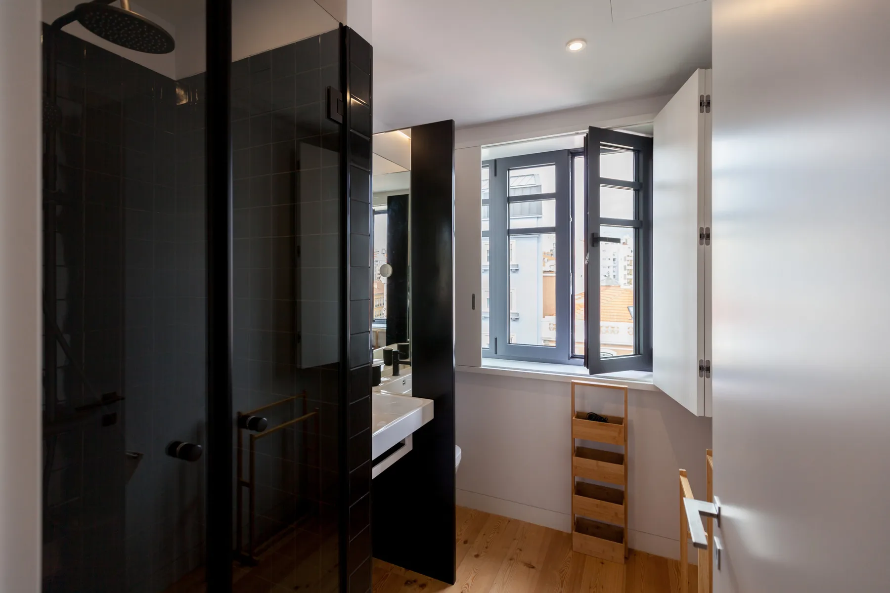 A bright bathroom with a shower, sink, and open window.