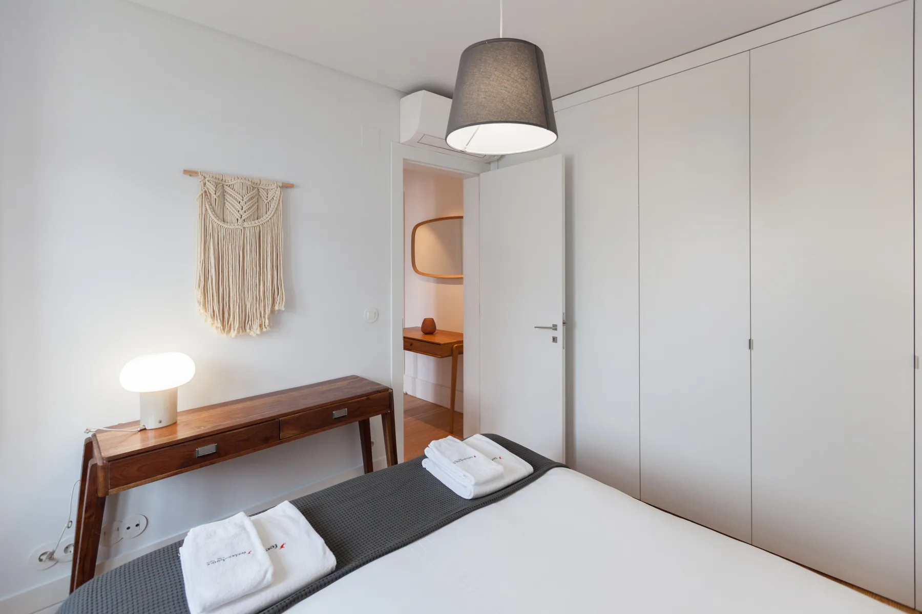 A bedroom with a bed, a wooden desk, and built-in wardrobes.