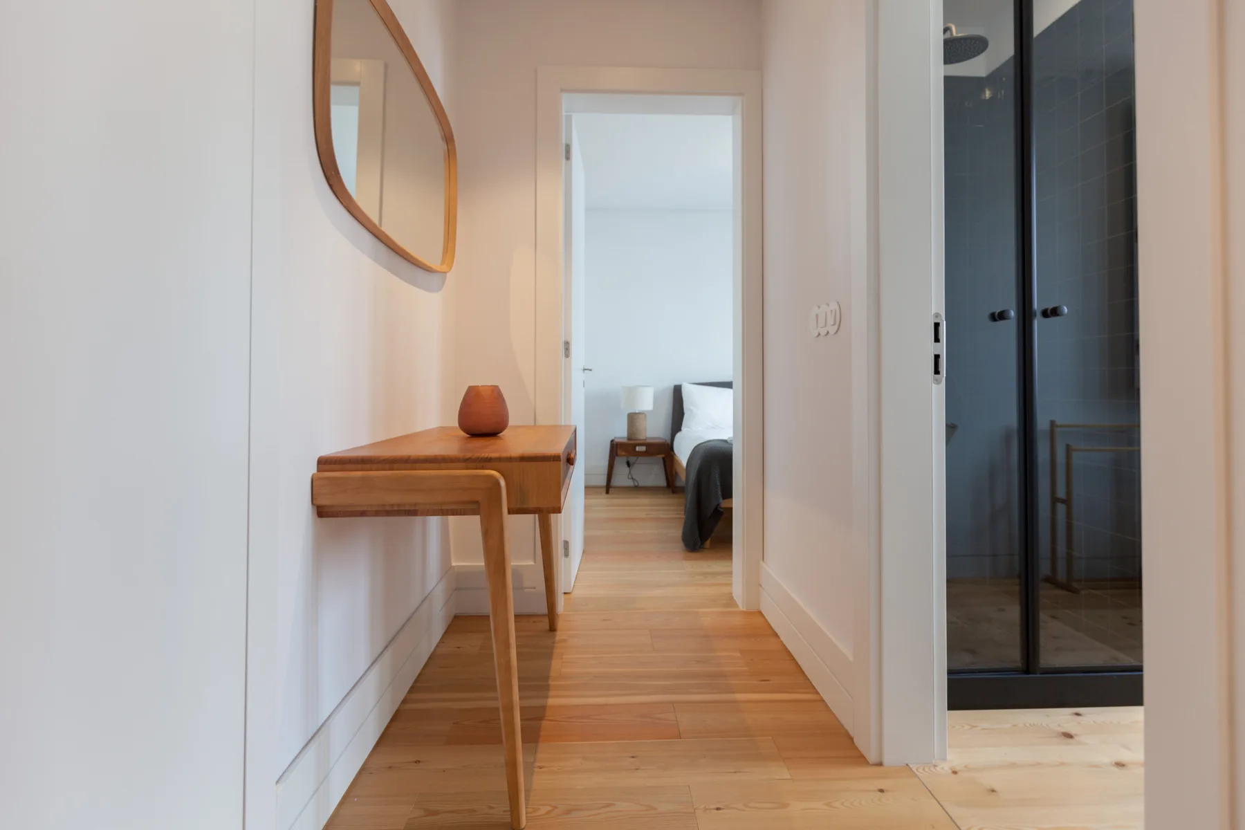 A bright hallway with wood flooring, a console table, and a bedroom doorway.