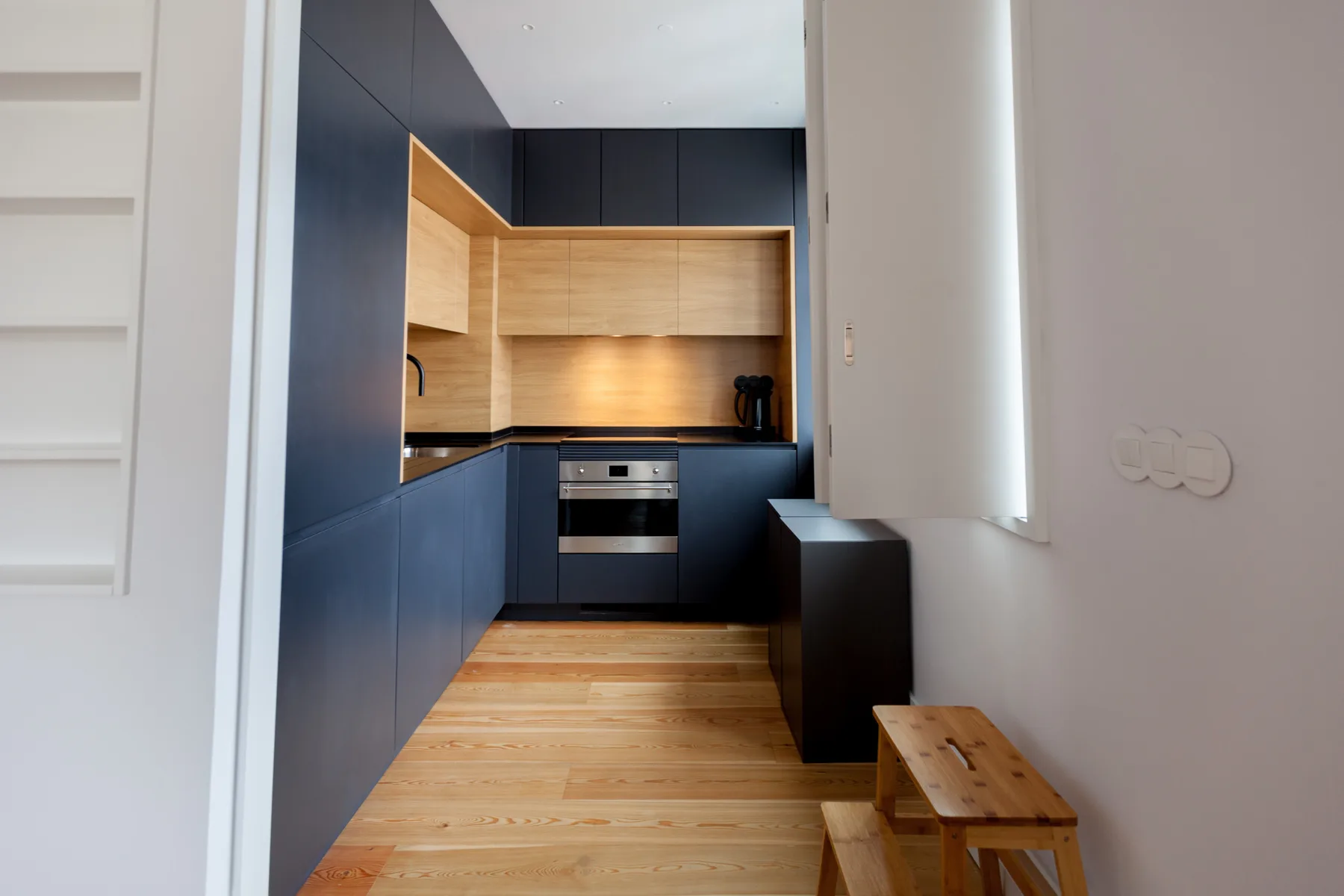 A modern kitchen with dark cabinets, light wood surfaces, and a built-in oven.