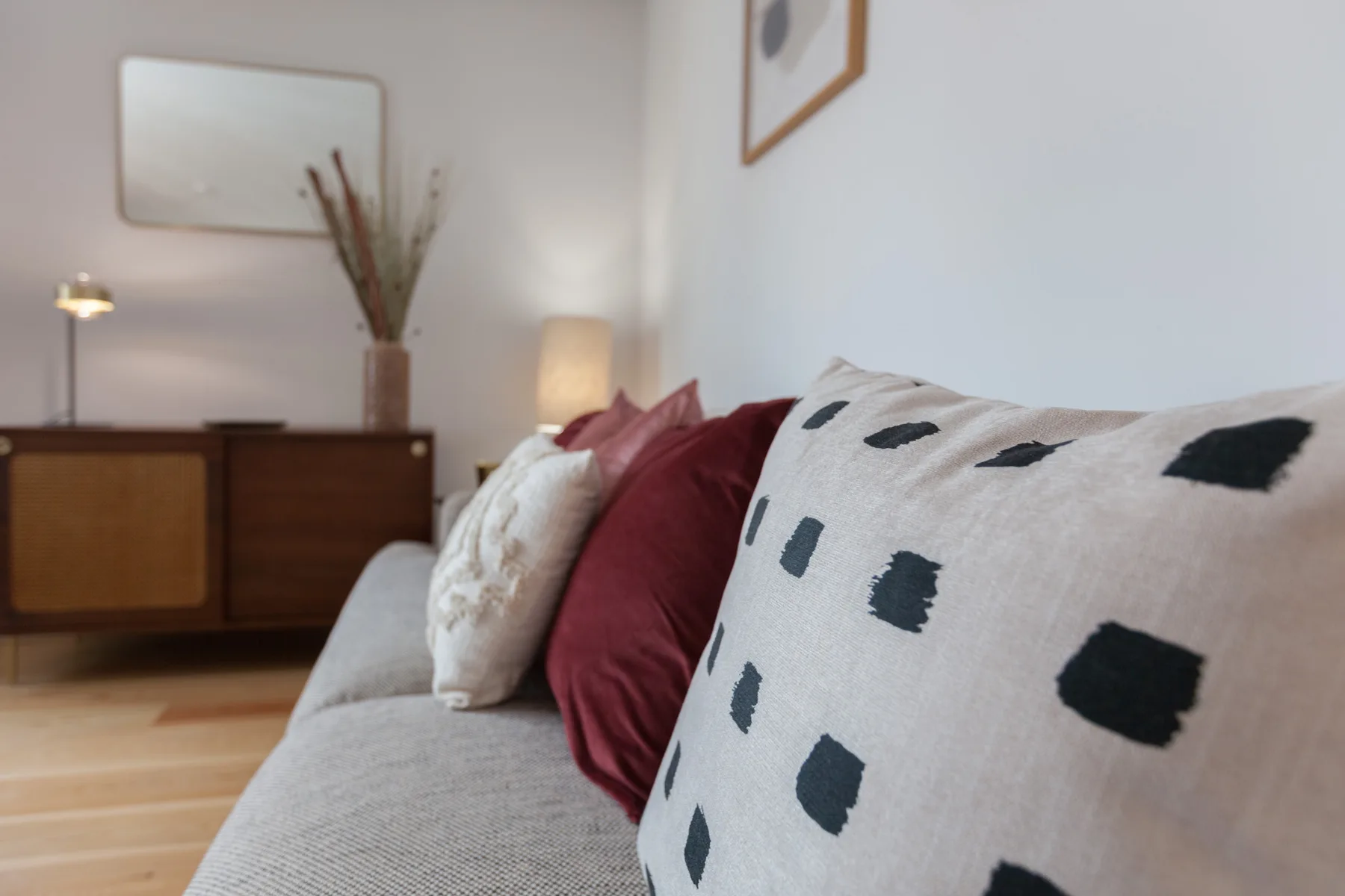 A living room with a gray sofa and patterned cushions beside a wooden cabinet.