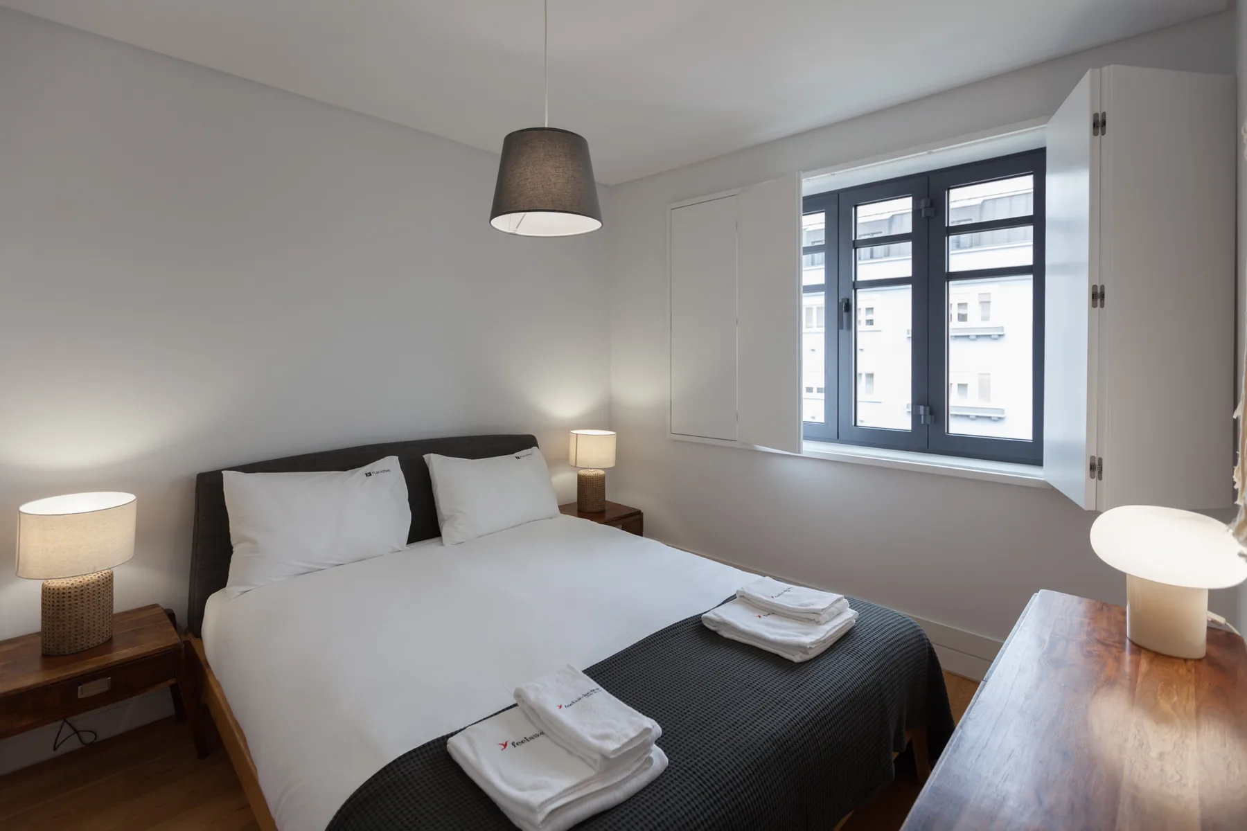 A bright bedroom with a double bed, bedside tables, and a large window.