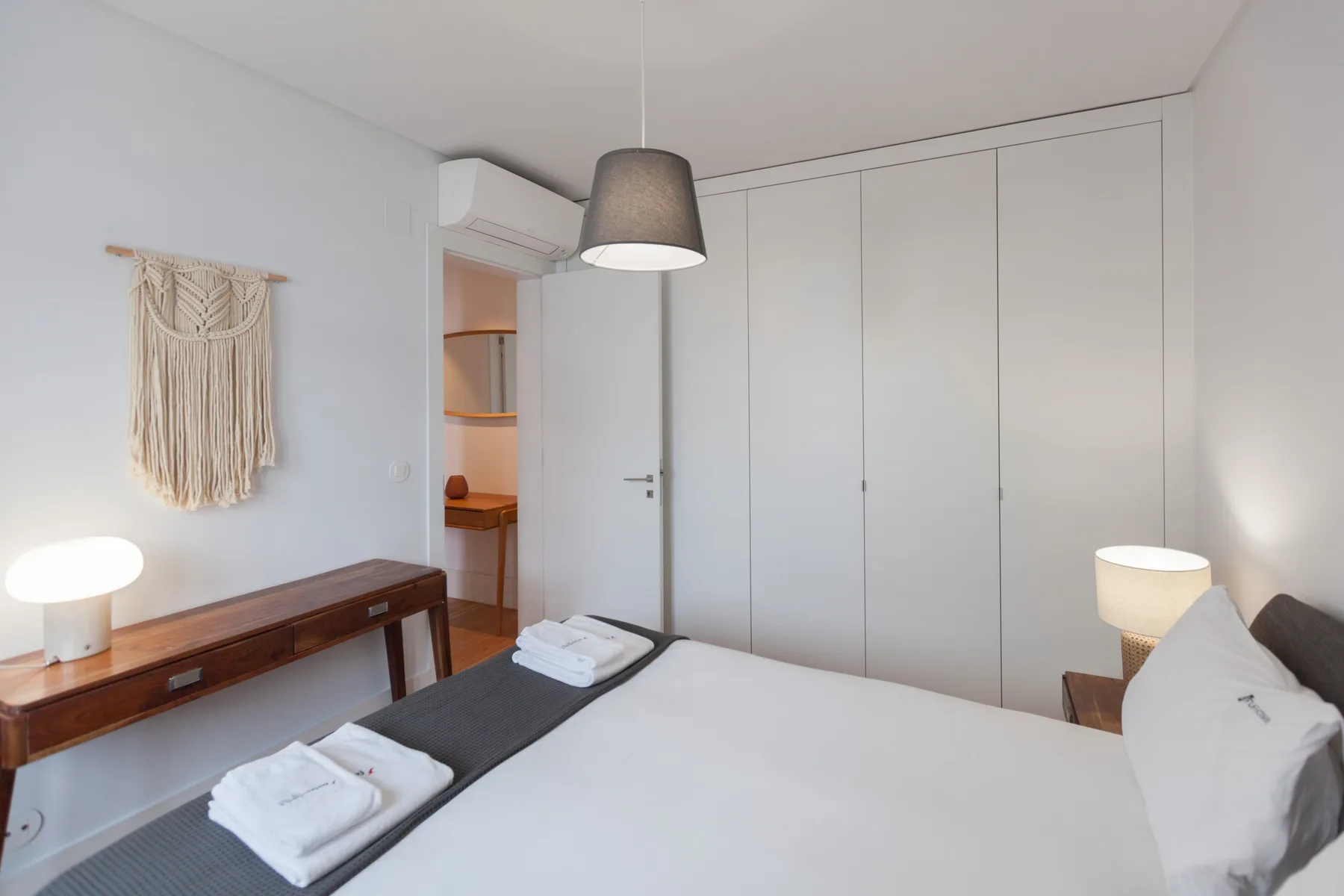 A bedroom with a bed, bedside lamps, and a wooden console table.