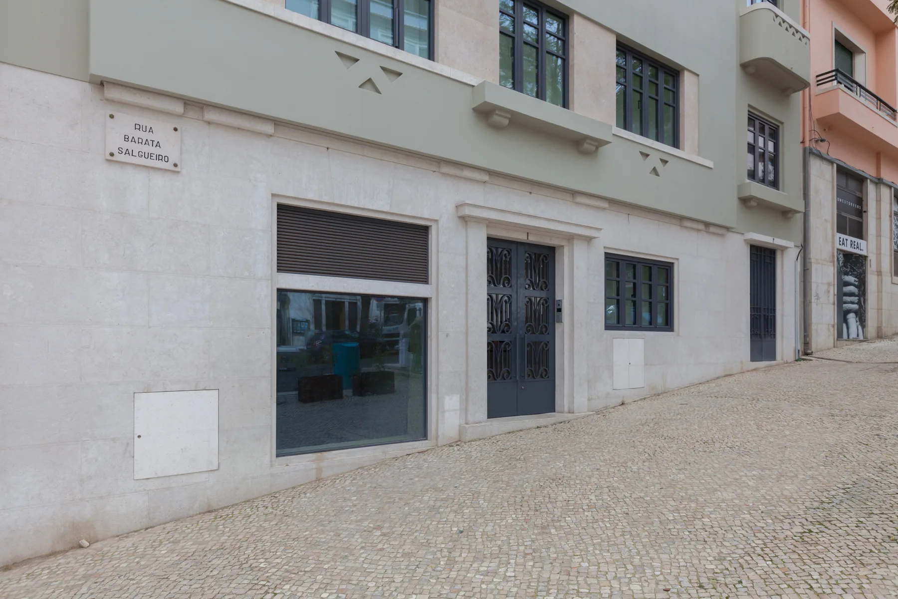 Street view of a pale building facade with a dark entrance and storefront window.