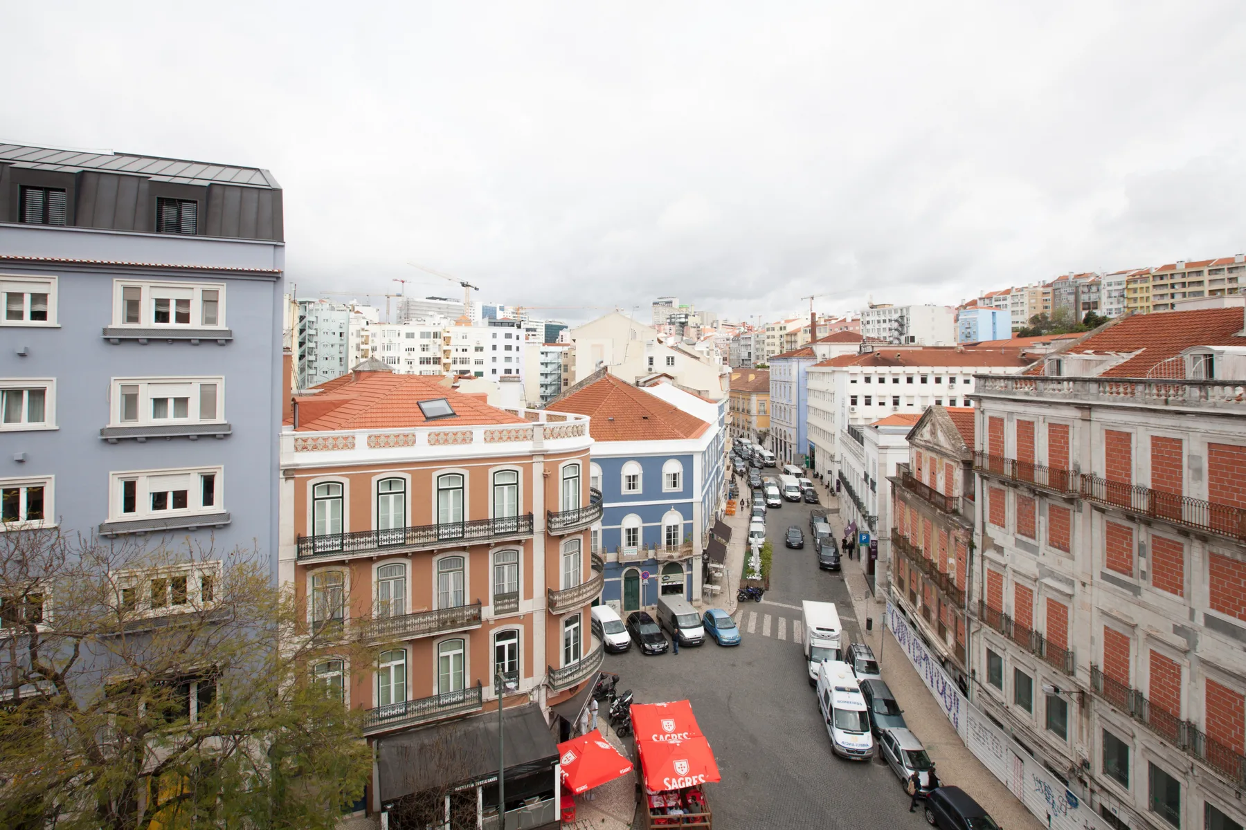 An urban street scene with colorful buildings and parked vehicles under a cloudy sky.