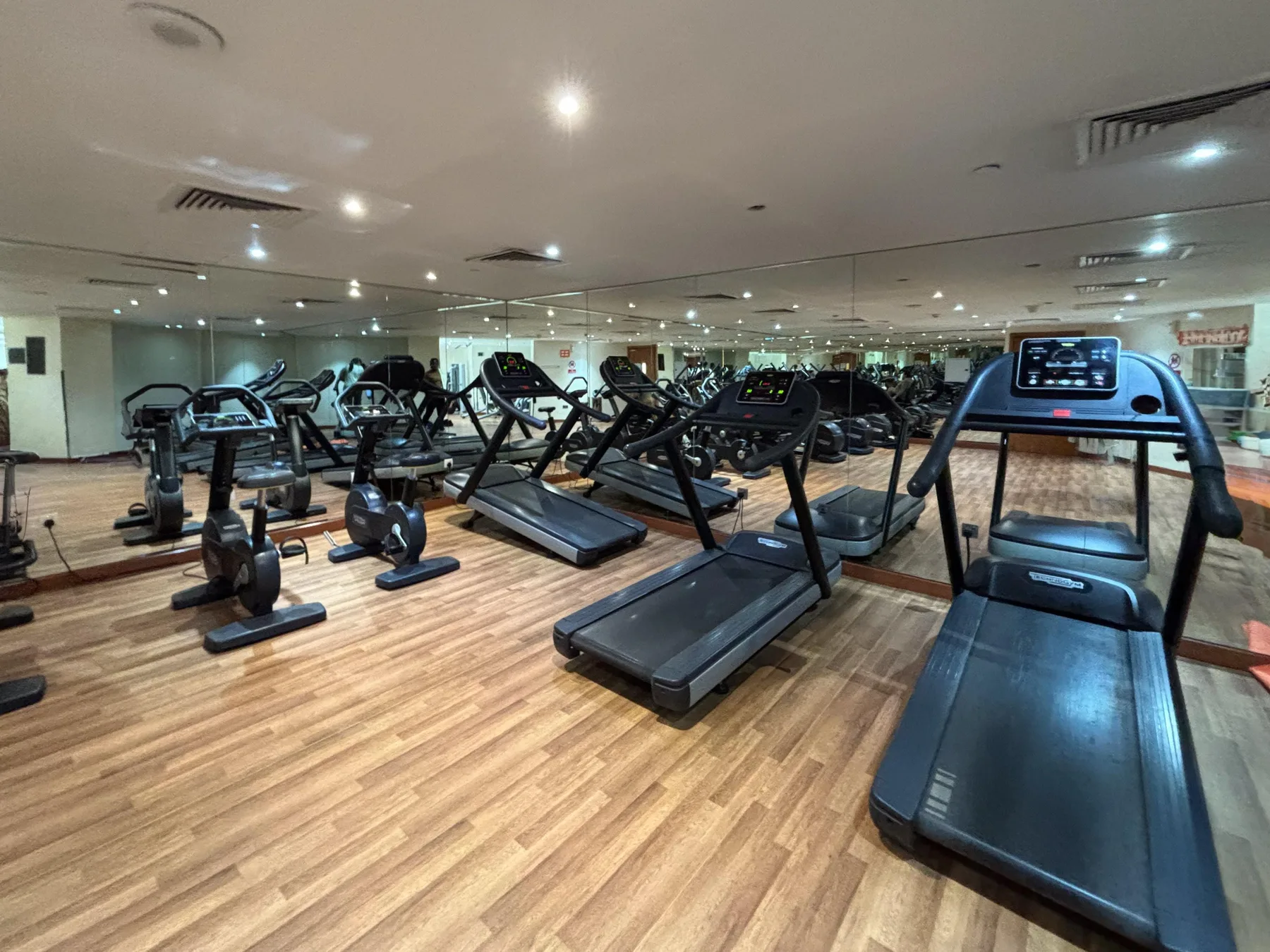 A gym with treadmills and other exercise equipment arranged across a wood-patterned floor.
