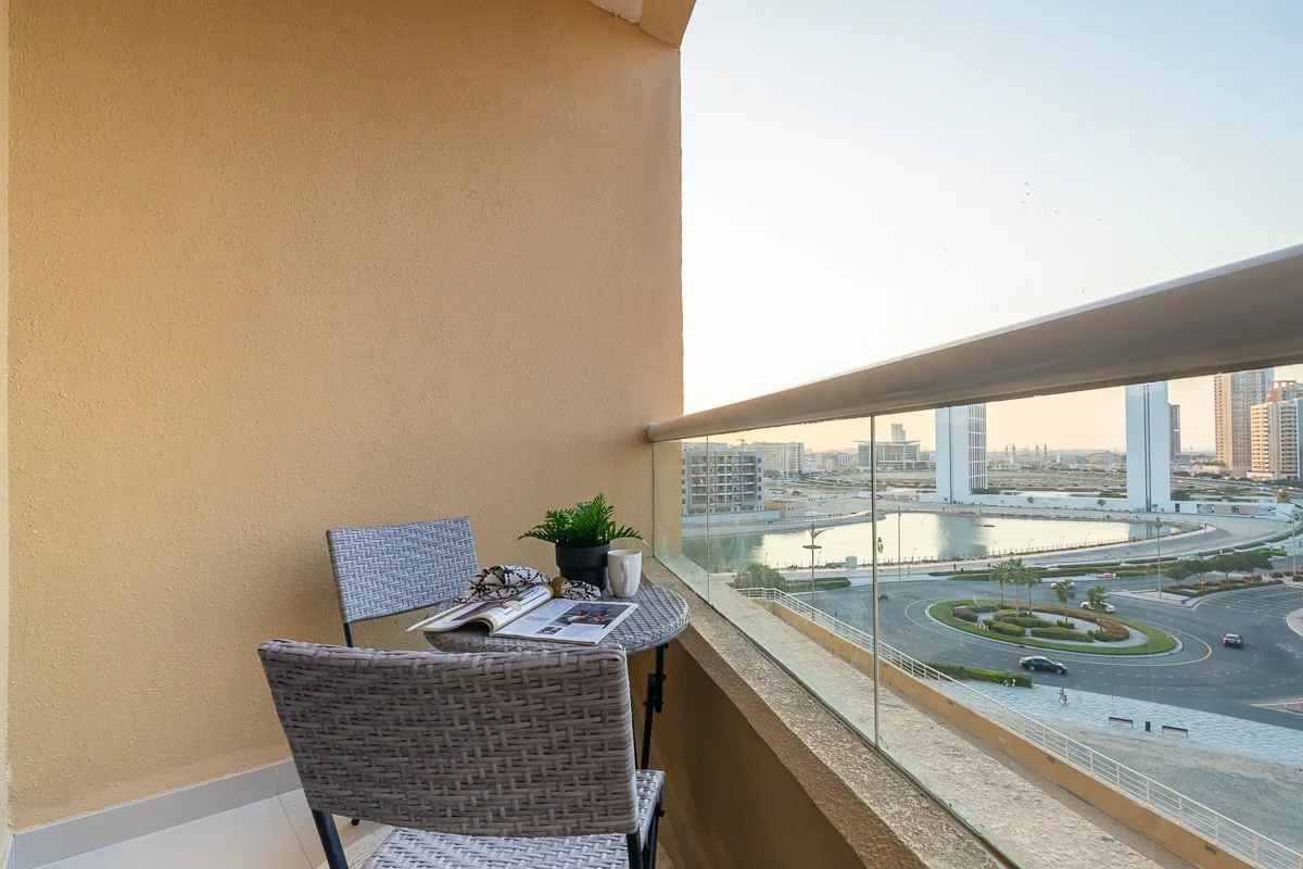 A small balcony seating area overlooks a landscaped roadway and distant buildings.