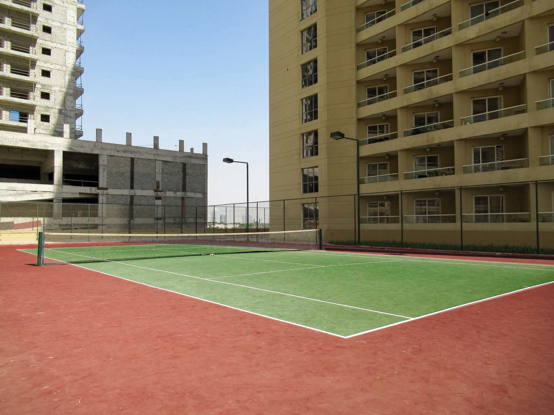 An outdoor tennis court sits between several apartment buildings.